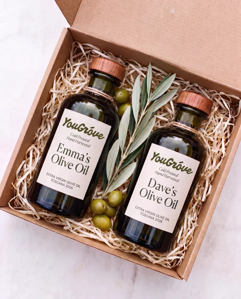 Two personalized YouGróve bottles nestled in a wood-wool gift box with olives and a sprig of olive leaves